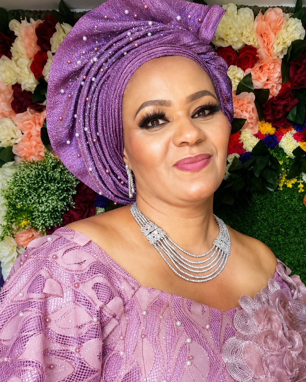MIO smiling in a purple gele and traditional celebration attire